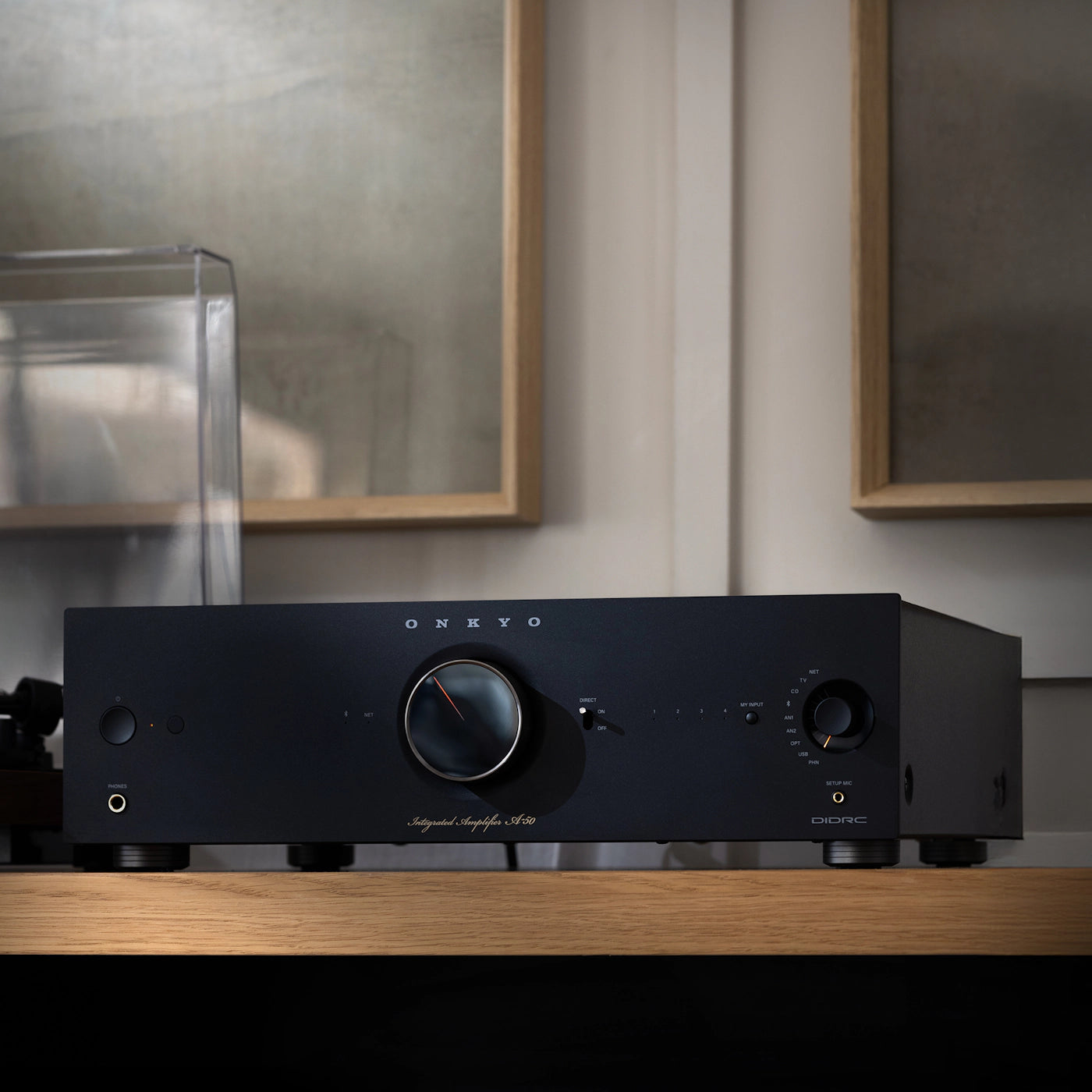 Black audio amplifier on a wooden surface with framed pictures in the background