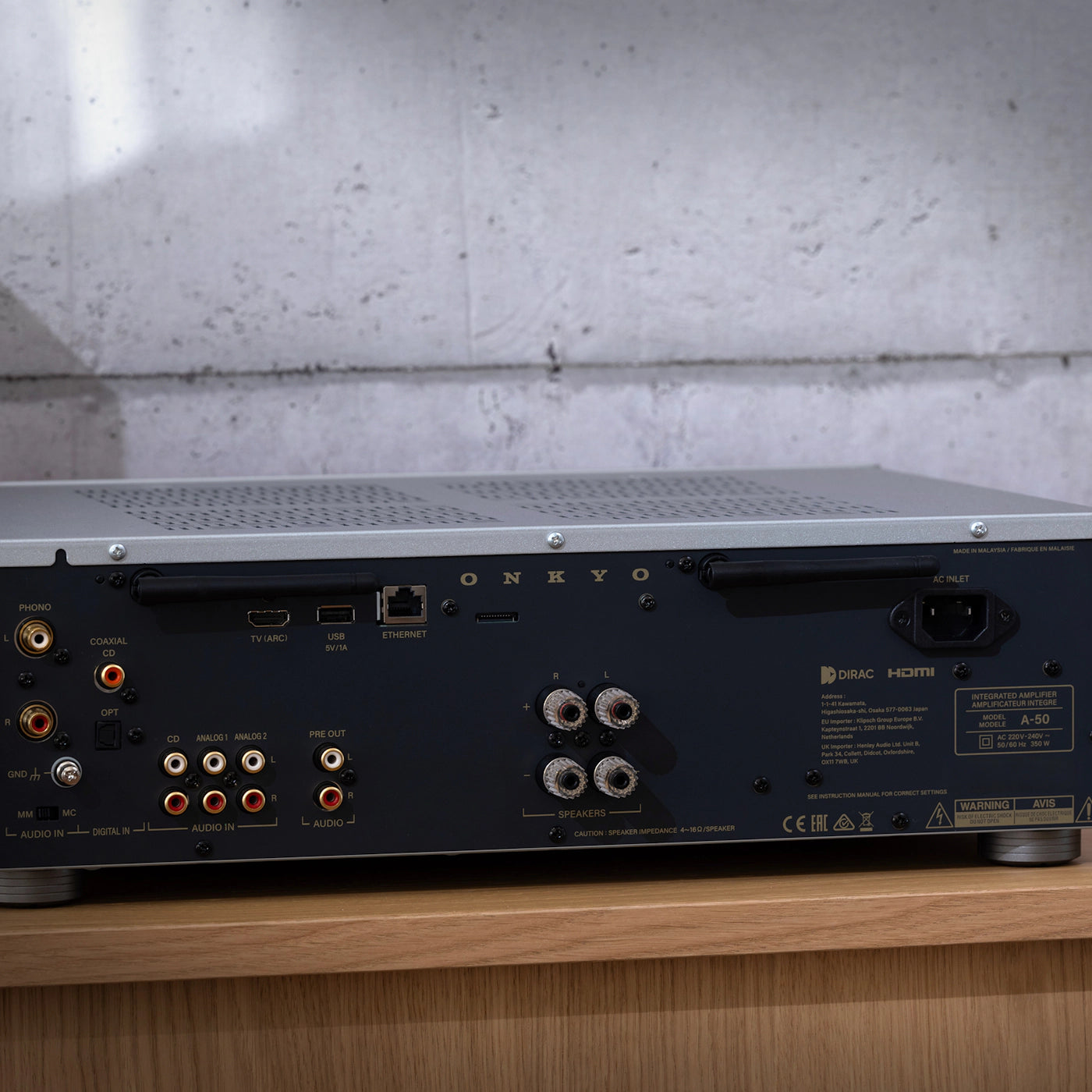 Back view of an audio equipment unit on a wooden surface with a concrete wall background